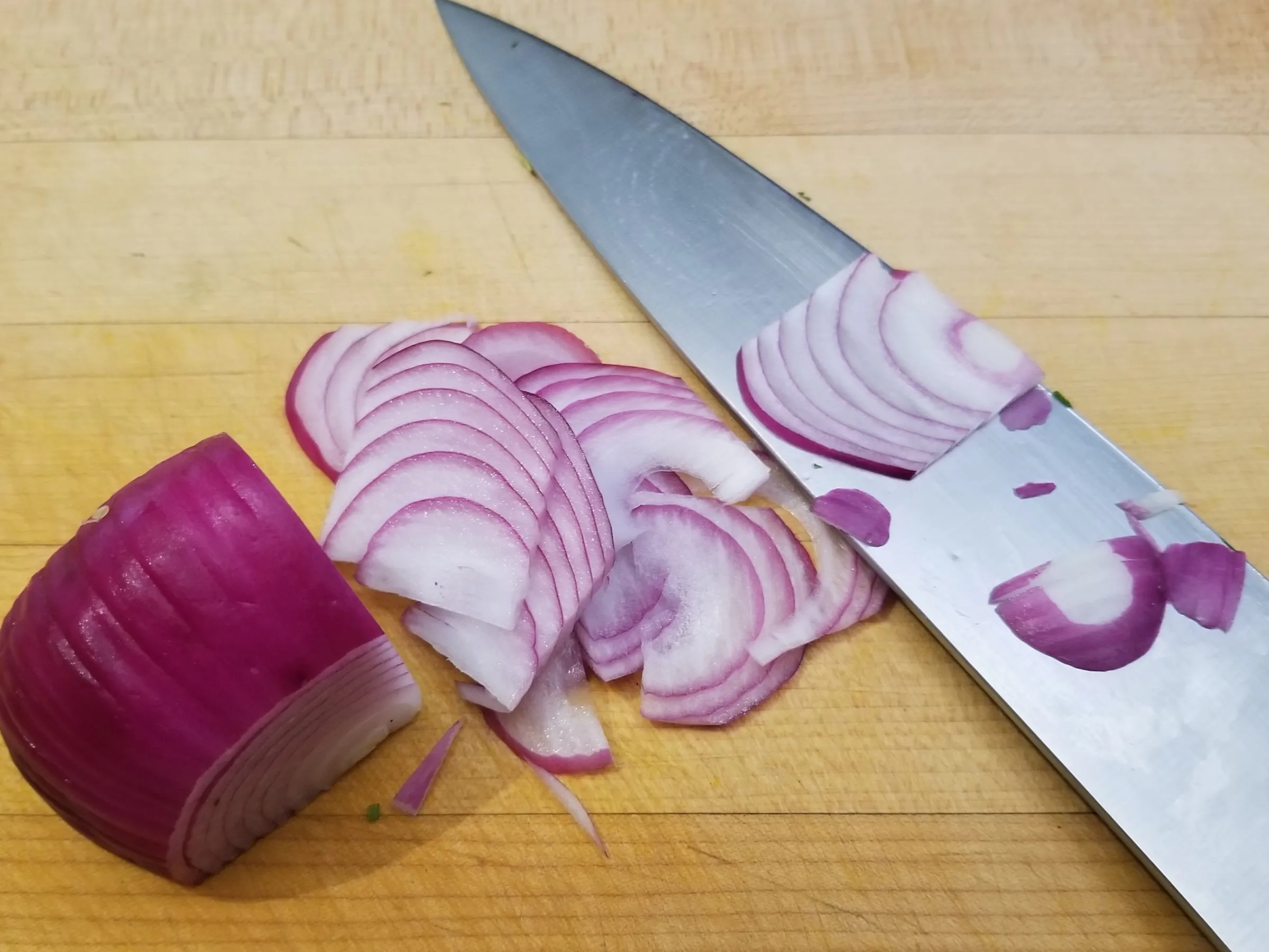 Sliced red onion and knife on a wooden cutting board.