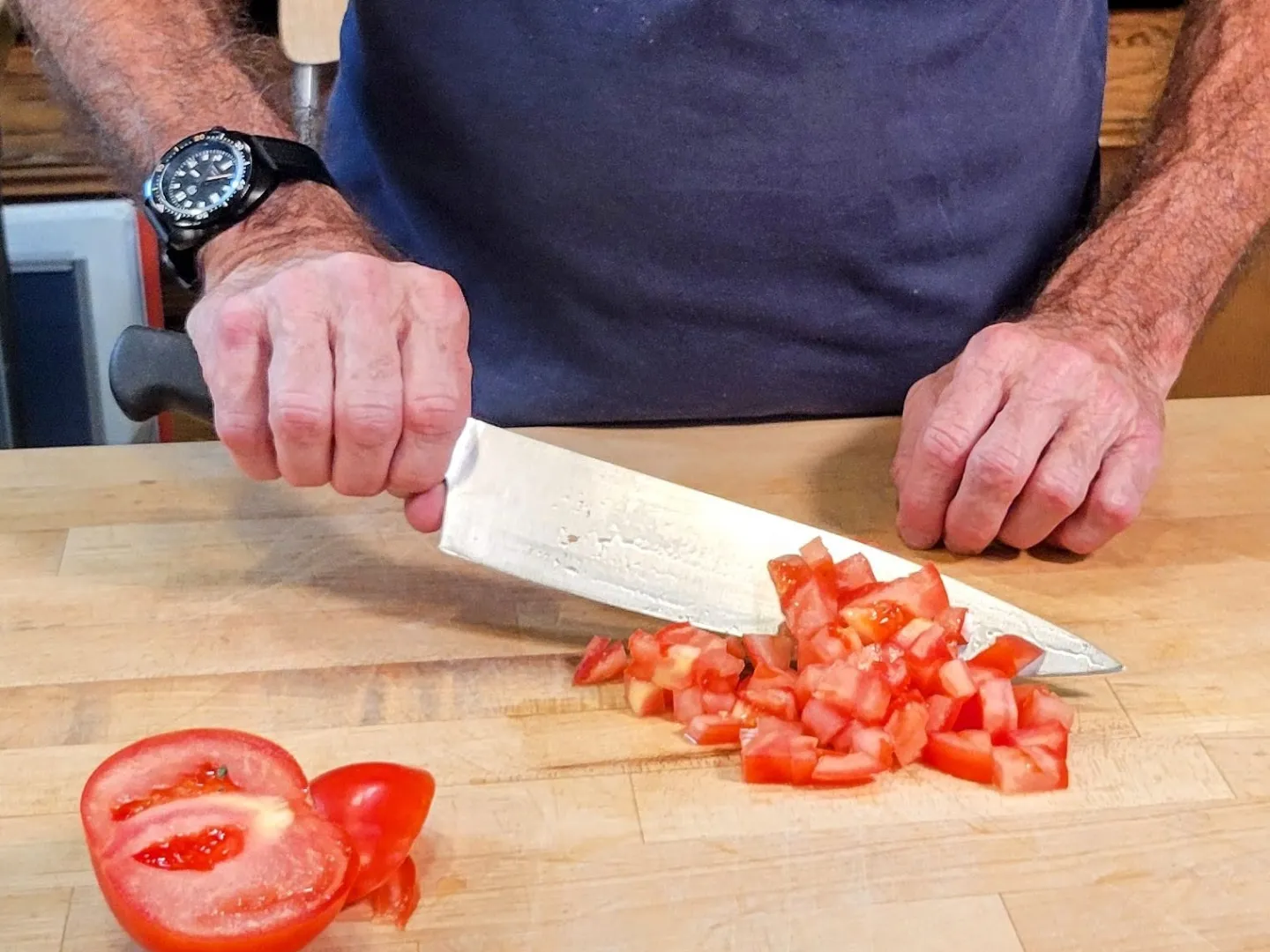 Person chopping diced tomatoes on a wooden cutting board with a large knife.
