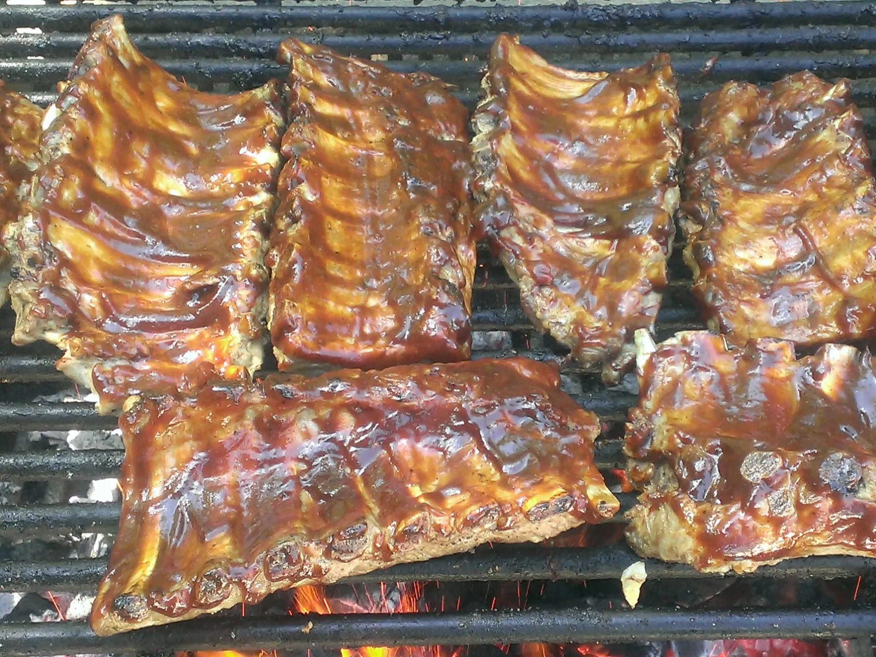Ribs covered in barbecue sauce grilling on an open flame barbecue.