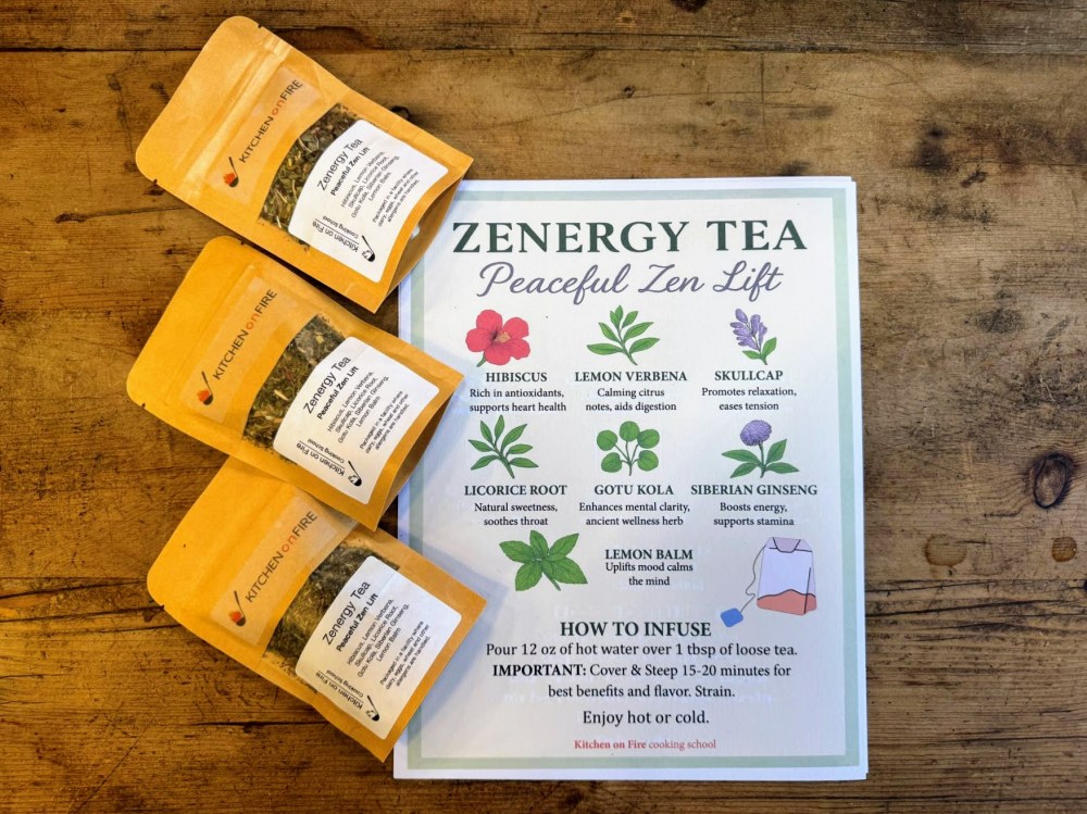 Three tea packets beside a Zenergy Tea info sheet with herb benefits on a wooden table.